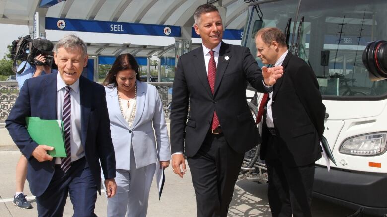 Four people stand in front of a bus at a transit stop.