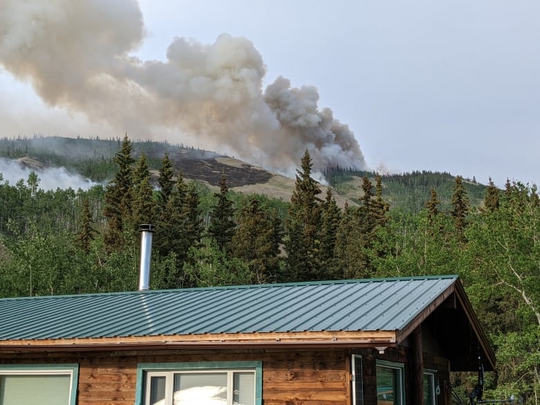 Smoke from a forest fire is seen in the mountains near a cabin.