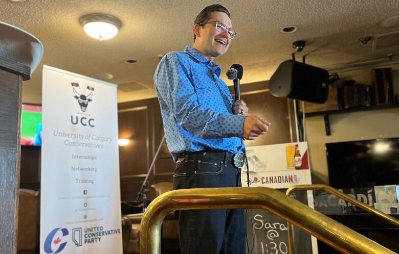 A smiling bespectacled politician dressed in a western shirt speaks into a microphone.