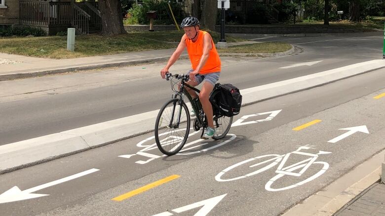 Man wearing a helmet rides bicycle over bike painted in white on road to indicate a bike lane.