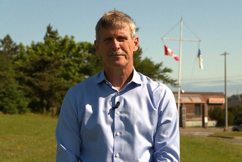 A person wearing a blue dress shirt stands outside on a sunny day.