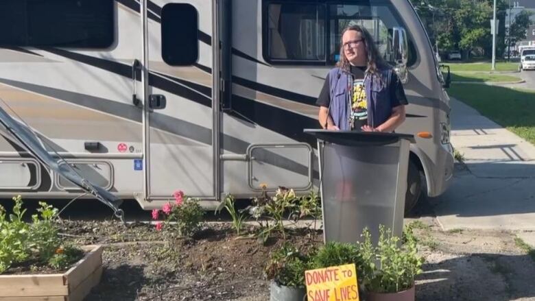 A person stands at a podium in front of an RV.