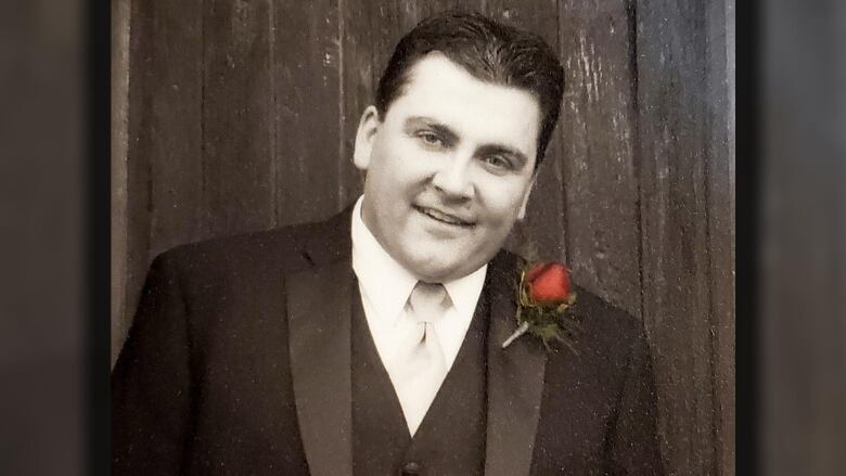 A portrait of a man wearing a formal suit with a red flower boutonnire on his suit jacket.