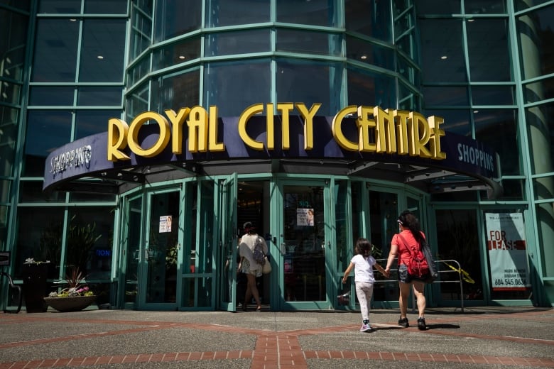 A mother and child, holding hands, enter a shopping centre called 'Royal City Centre'.