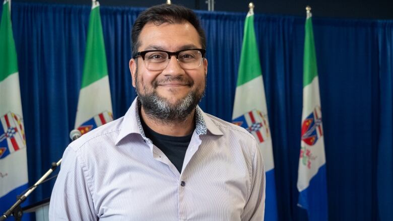 A portrait of a man smiling with flags behind him.