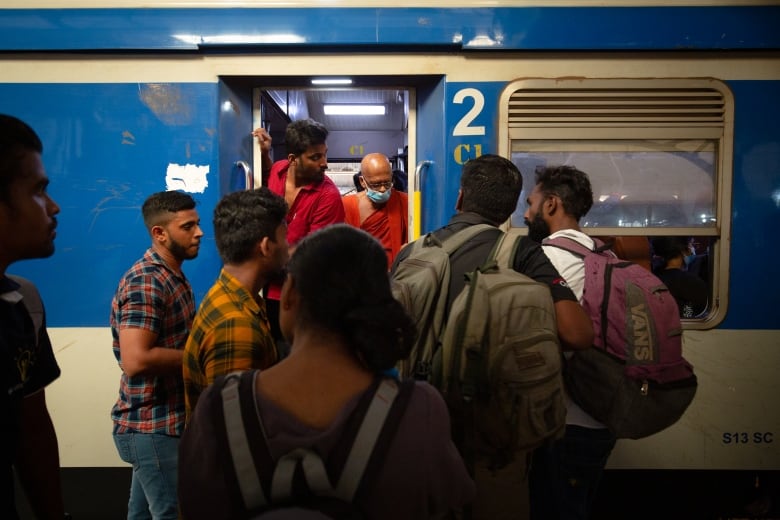 Several people, some with backpacks are shown lining up to board a train.