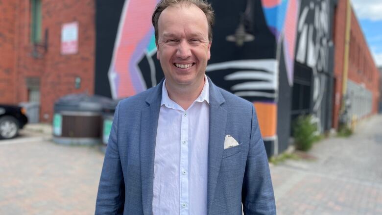 A smiling man in a suit standing in front of a mural.