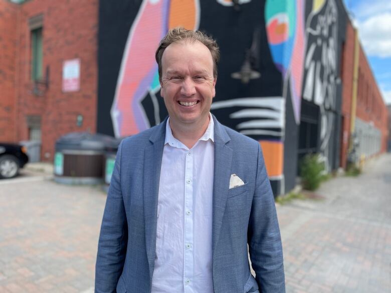 A smiling man in a suit standing in front of a mural.