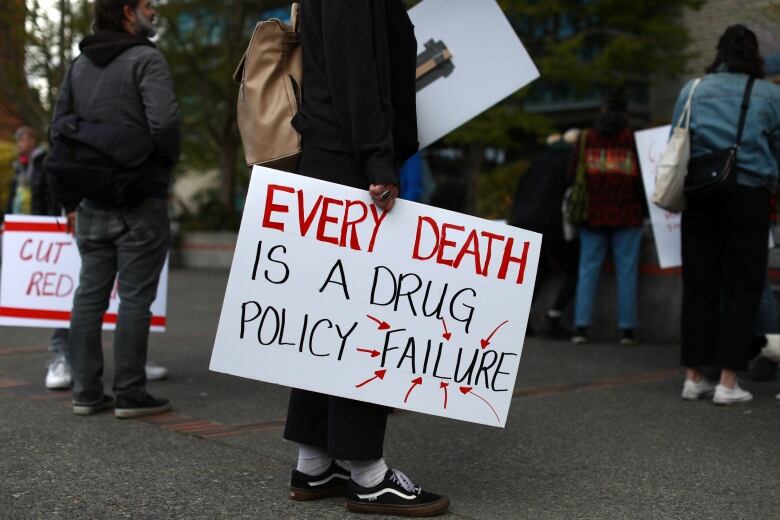 A protester holds up a sign that reads 'Every Death is a Drug Policy Failure'.