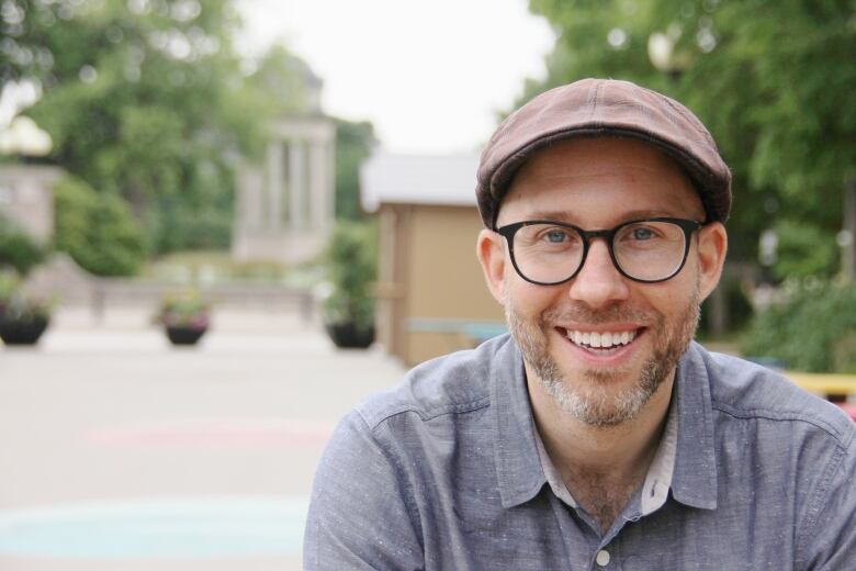 Portrait of man with a beard wearing glasses, a hat and a blue button-up shirt.