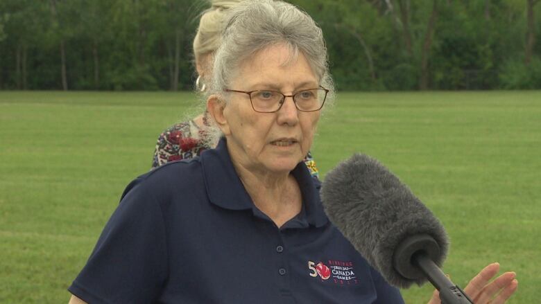 A woman speaks into a fuzzy microphone outside.