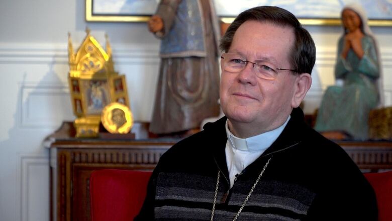 A priest sitting in front of a drawer with religious artifacts.