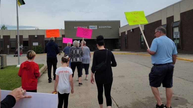 A group of people with coloured signs walk toward the entrance of the Kamsack Hospital in Kamsack, Saskatchewan.