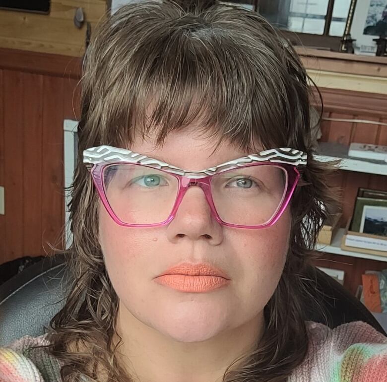 A woman with light brown hair wears bright pink glasses.