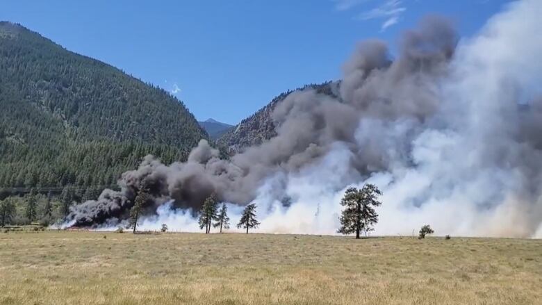 Smoke rises across a field as the out-of-control Nohonim Creek wildfire burns 1.7 km northwest of Lytton B.C.