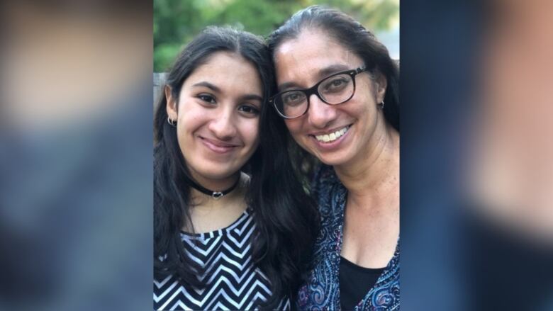 A teenager and woman with glasses are smiling into the camera.