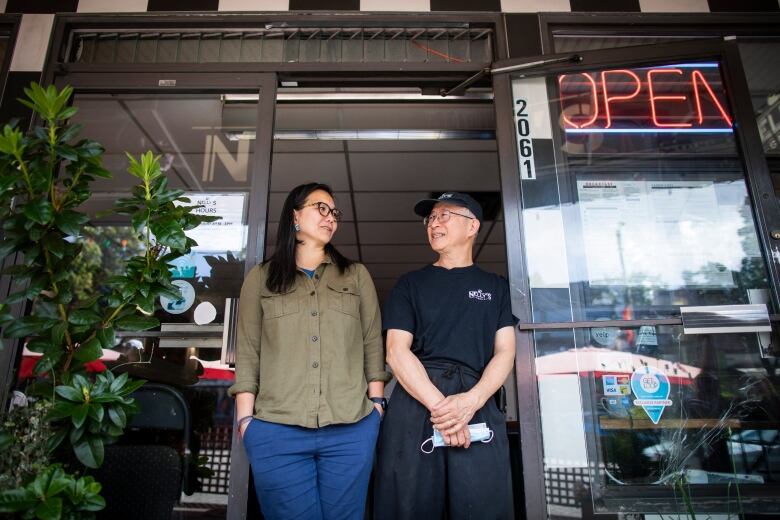 Joyce and Nelson look at each other at the front door of Nelly's Grill. They are both wearing glasses.