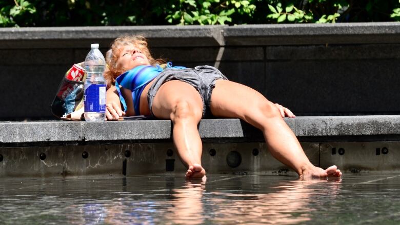 A woman lies on the ground with her feet in water.