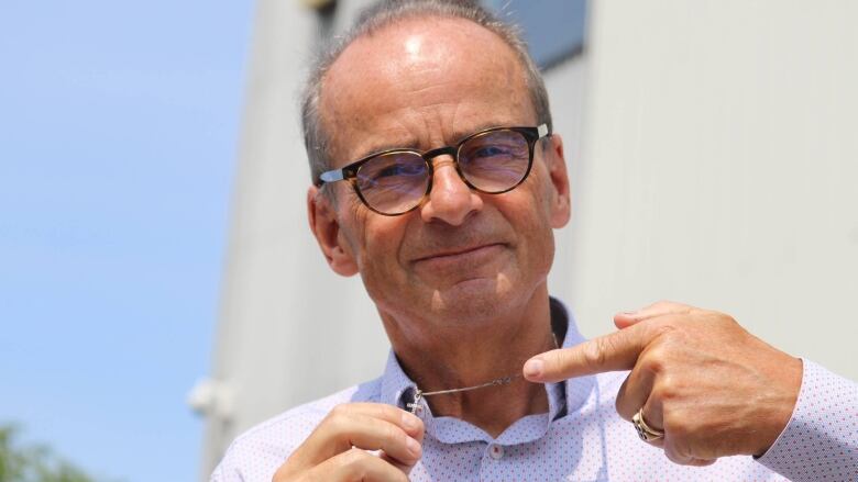 A smiling man holds up the tiny crucifix on the chain around his neck.