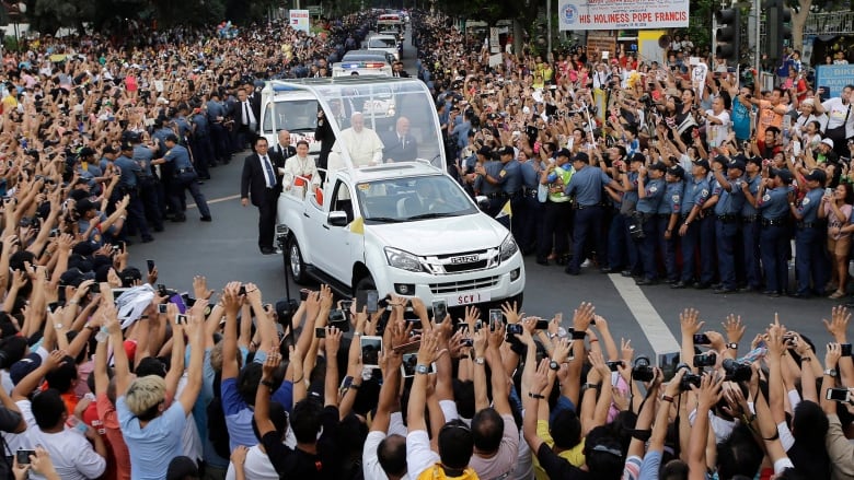 Crowds of Filipinos with arms raised as the white Popemobile passes by.