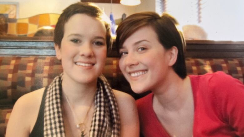 Two women sit in a restaurant booth and smile at the camera.