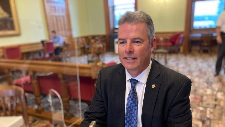 A man sits before a microphone inside the New Brunswick Legislature.