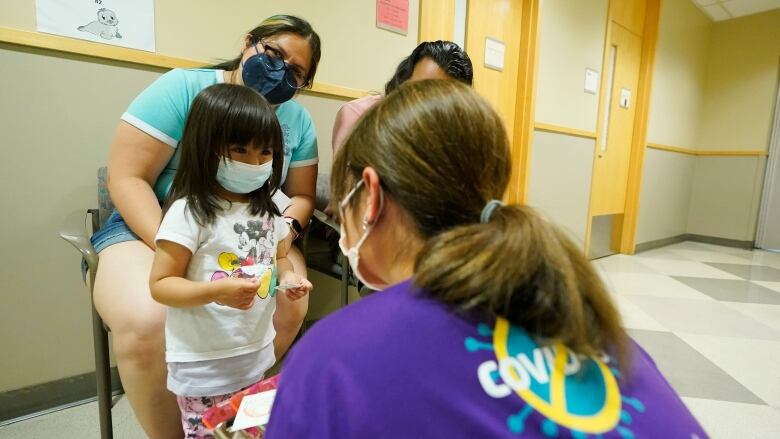 A little girl wearing a mask with three adults smiling.