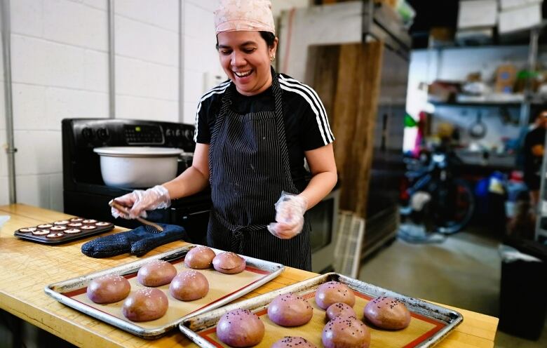 Woman at farmers' market stall with buns for sale.