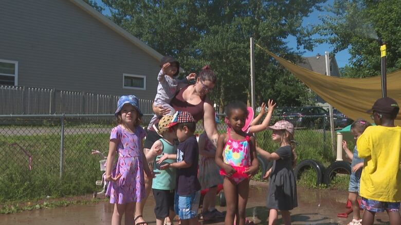 Group of young children with instructor, playing outside. Instructor is holding a very small child.