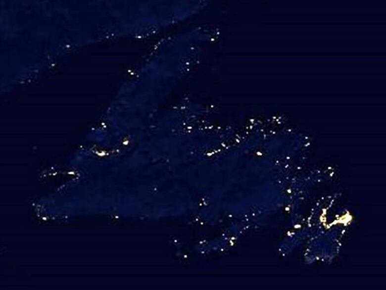 A photograph from space shows the island of Newfoundland at night. Bright white dots are speckled throughout the island, with concentrations in urban area, particularly on the northeast Avalon Peninsula. 