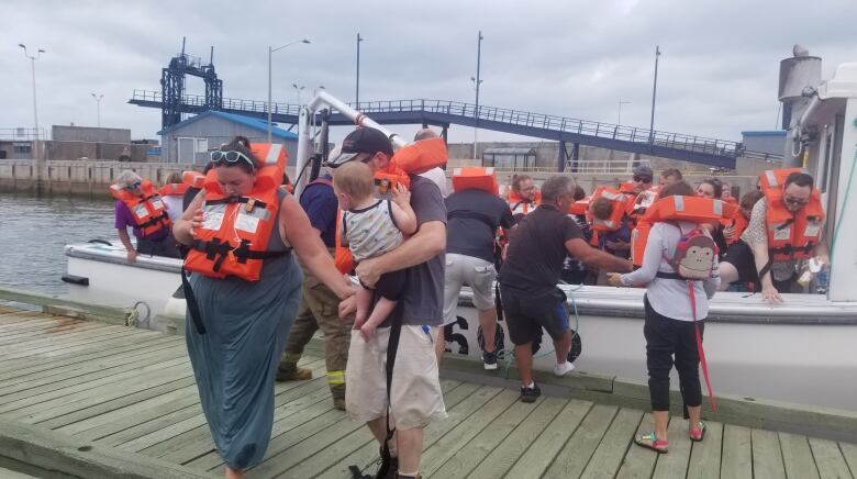 a group of people wearing life orange life jackets are getting off a boat and onto a wooden dock