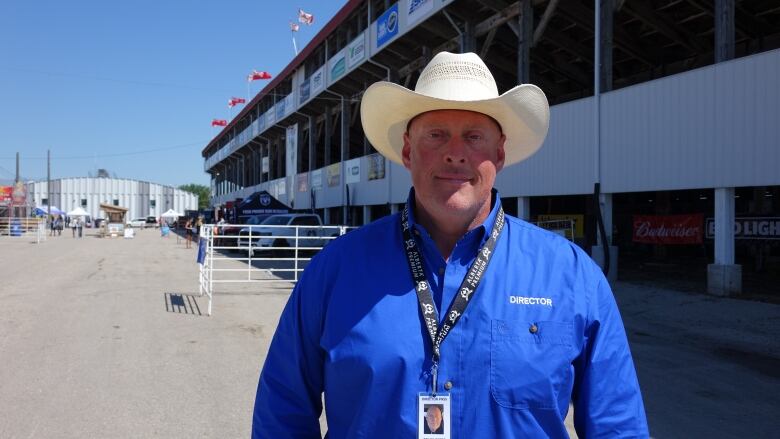 A man in a blue shirt and a cowboy hat smiles.