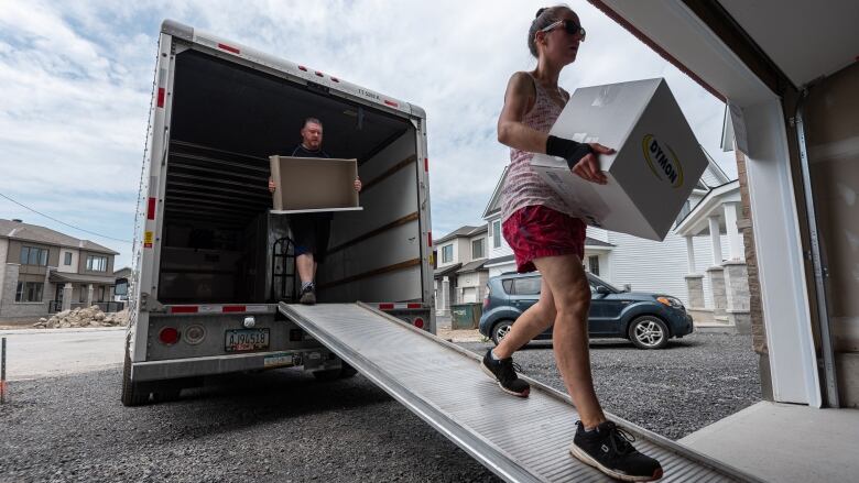 Man and woman carry boxes down a ramp out of a moving van. 