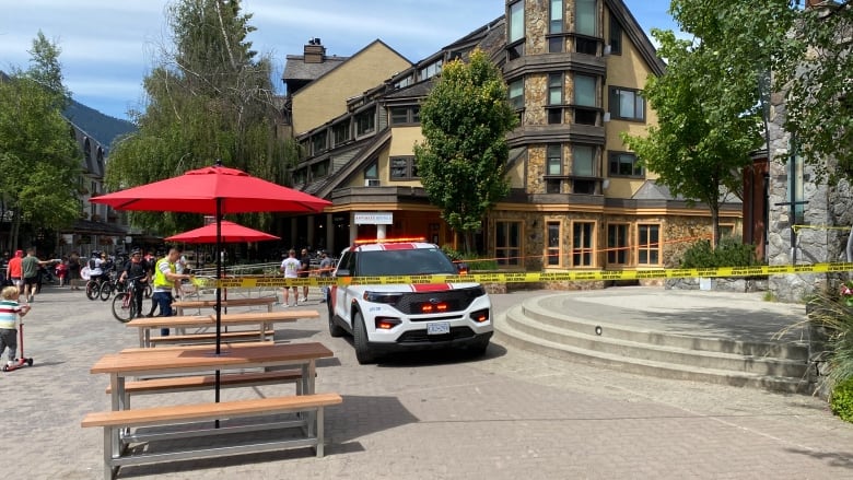 A red car with a siren on it behind police tape in a pedestrian plaza.