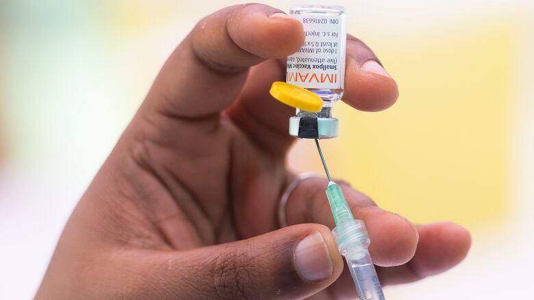 A hand holds the monkeypox vaccine and a syringe.