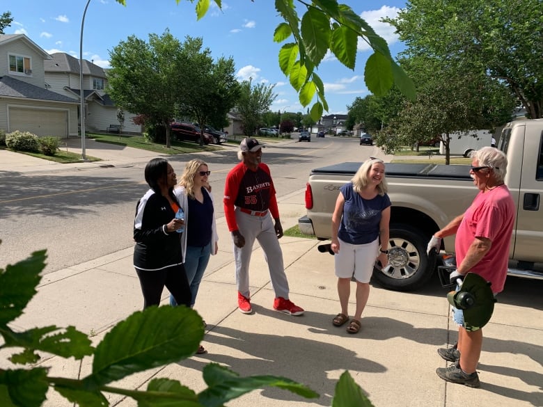 A group of five people stand around talking on a driveway.