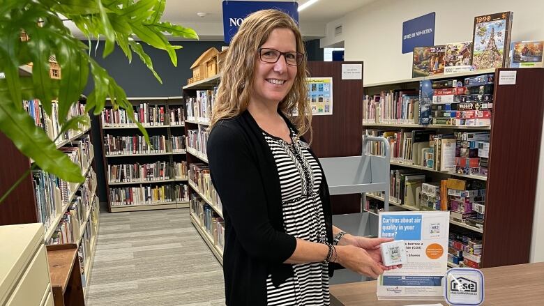 A woman in a library holds a small carbon dioxide monitor.