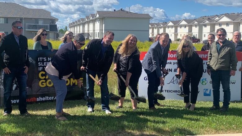 A group of people standing in a line holding shovels. 