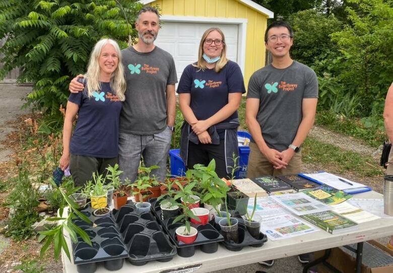 Four people stand in front of a table with plants on it.