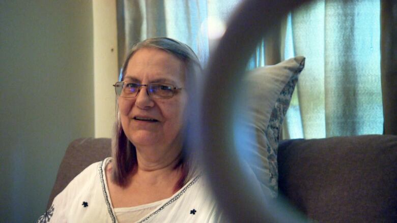 A woman in glasses sits on a couch and looks into the camera, and a grab bar in the foreground.