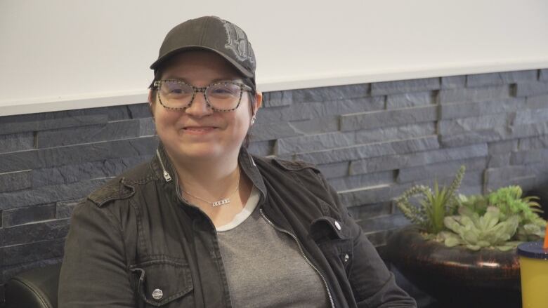 A person in a baseball cap and glasses smiles.