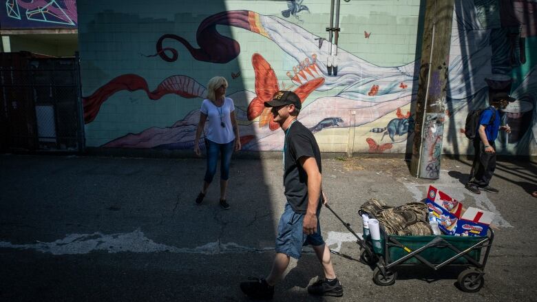 A man dragging a cart along a street, with a painted mural in the background.