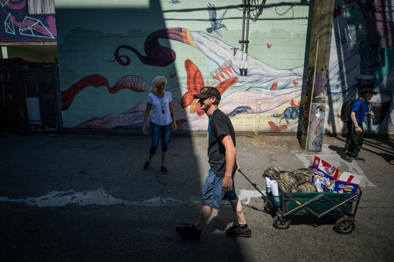 A man dragging a cart along a street, with a painted mural in the background.