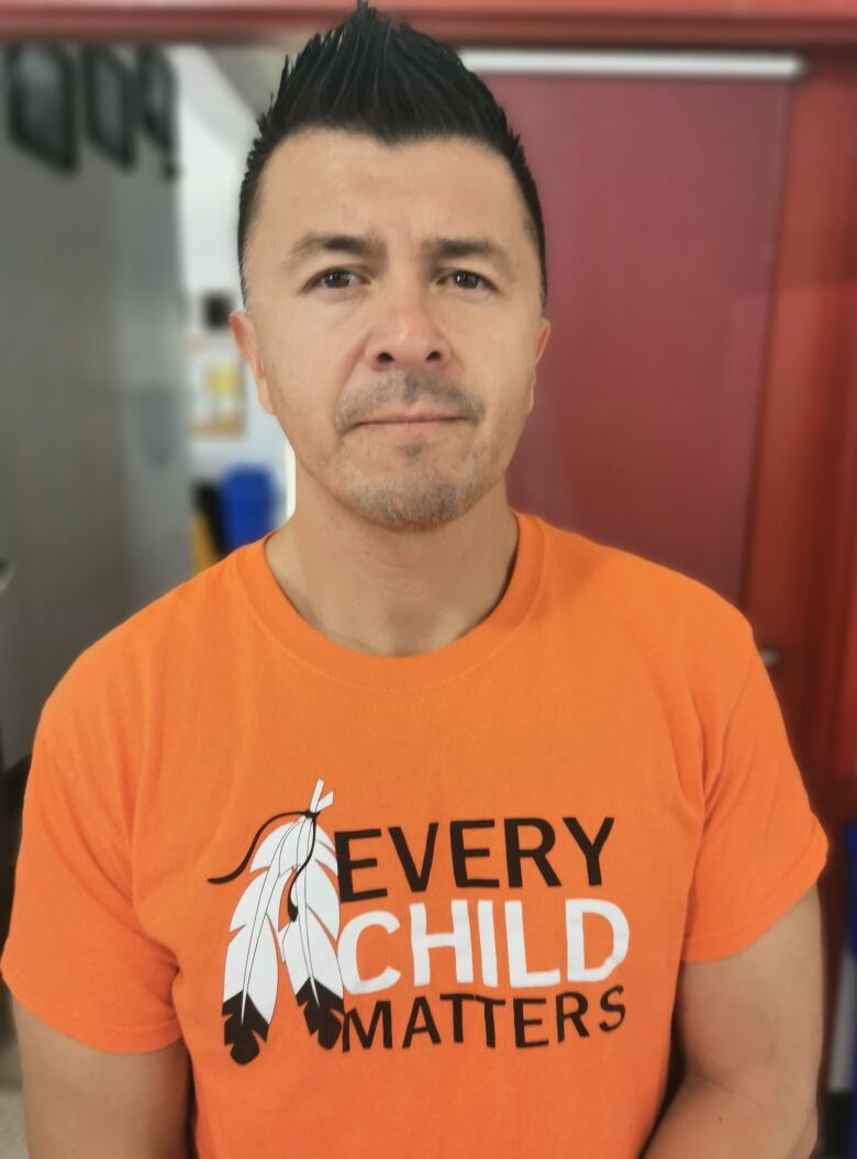 Man in Every Child Matters orange t-shirt looks art the camera.