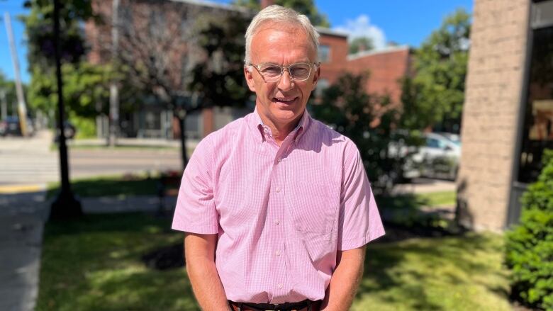 Sean Casey stands on Charlottetown street on a sunny summer day. He is wearing a short sleeved pink dress shirt. 