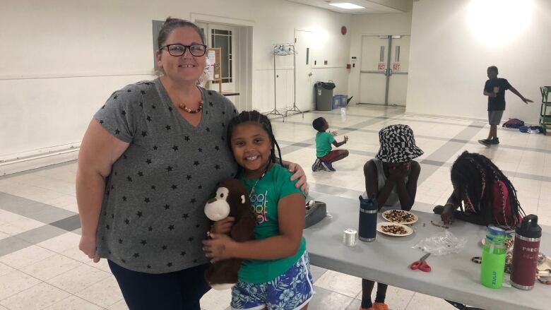 A woman stands beside a child, with an arm wrapped around the child.