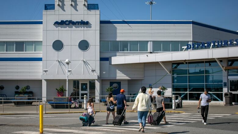 A number of people with luggage approach a B.C. Ferries terminal.