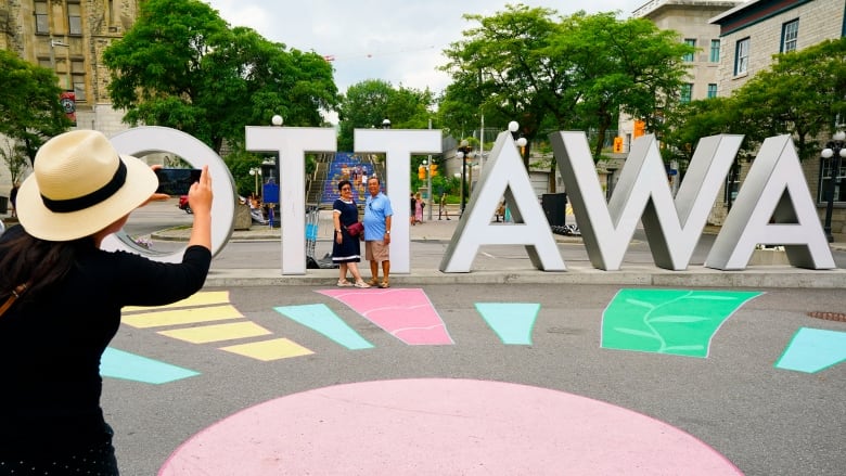 A person takes a photo of two people standing in front of a large 