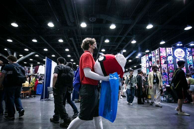 A masked person walks through a crowded convention floor.