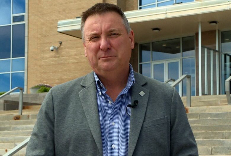 A person wearing a blue shirt and blazer stands on the steps of Confederation Building.